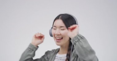 Asyalı kadın, kulaklıklar ve müzik eşliğinde dans. Stüdyoda öğrenci sağlığı, canlı yayın hizmeti ve Kpop şarkısı. Beyaz arka planda ses, elektronik ve enerjiyle dinleyen genç Koreli..