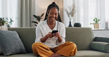 Kanepede oturan siyahi bir kadın, gülüyor ya da telefonda meme, sosyal medya ya da blogda gülümseyen bir yazı yazıyor. Akıllı telefonlu mutlu kız e-postaları, komik web sitelerini ya da oturma odasında online sohbeti kontrol ediyor..