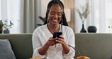 Kanepede oturan siyahi bir kadın, rahat ol ya da telefondaki mim, sosyal medya ya da blog yazısını evinde gülümseyen bir şekilde yaz. Akıllı telefonlu mutlu kız e-postaları, komik web sitelerini ya da oturma odasında online sohbeti kontrol ediyor.
