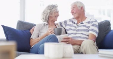 Kahve, sohbet ve kanepede oturan içki içen, sohbet eden ve evde sohbet eden yaşlı bir çift. Evlilik, emeklilik ve mutlu kadın ve erkek bağlılık, ilişki ve oturma odasında rahatlama..
