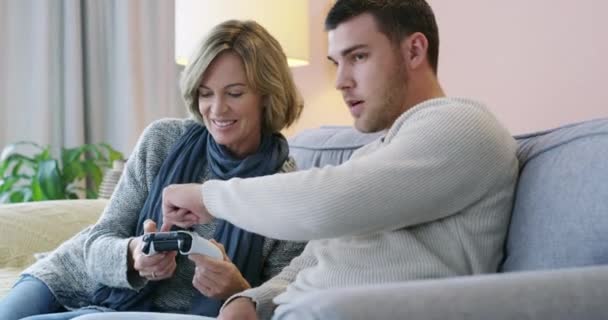 年轻男子 母亲和沙发教学控制器按钮的视频游戏或粘连在客厅在一起的家 快乐的男人 给妈妈展示游戏的控制权 — 图库视频影像