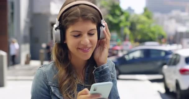 ソーシャルメディアで音楽やネットワーキングを聞く街のヘッドフォンを持つ電話 ダンス カナダ出身の笑顔 女性が街の携帯電話でプレイリスト ラジオ アルバムをストリーミング — ストック動画