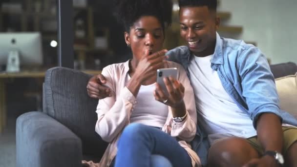 电话和快乐的夫妻在家里通过社交媒体 网络搜索或阅读网站信息来放松自己 非洲妇女和男子坐在沙发上 带着滑稽的迷因 新闻或在客厅里用手机聊天 — 图库视频影像