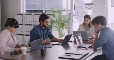 Bir grup iş analisti online fikirleri tarıyor ve bir toplantıya hazırlanmak için yeni sistemleri test ediyor. Ciddi ve çeşitli gençler bir ofisteki toplantı masasının etrafında dizüstü bilgisayarlarla çalışıyorlar.