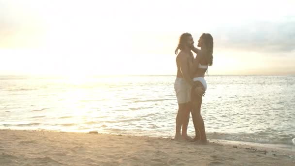 一对快乐的夫妇 拥抱并放松在沙滩上的夕阳西下 共度暑假或户外度假 男人在阳光下拥抱女人 寻求爱 拥抱或支持 自然是在海滨的海水边 — 图库视频影像