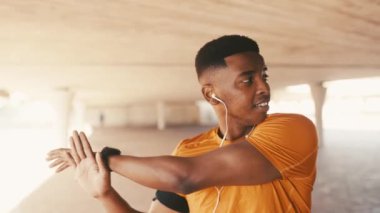 Siyahi bir adam, kollarını uzatıyor ve müzik için kulaklıklarla dışarıda egzersiz yapıyor. Sağlık, sağlık ve eğitim, ısınmak için radyo dinlemek ve egzersize başlamak, spor için spor yapmak..