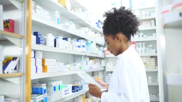 Μαύρη Γυναίκα Φαρμακοποιός Και Δισκίο Κουτί Στο Ράφι Για Φαρμακευτική — Αρχείο Βίντεο