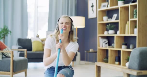 还有一个女人带着耳机在家里放音乐 以获得乐趣 精力和做家务活 在她的公寓里 年轻的女人带着快乐 快乐地拖地板 打扫地板 — 图库视频影像