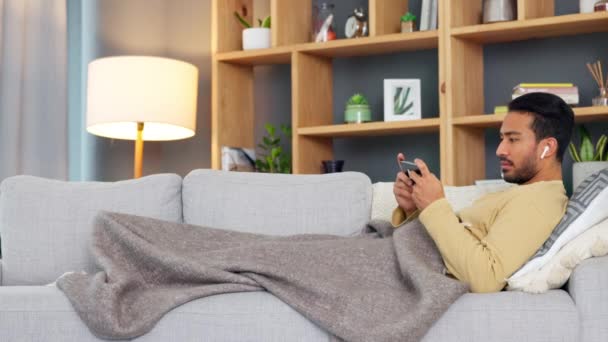 亚洲男人一边在家里一个人在沙发上打呵欠和放松 一边在网上看电影或电视剧 厌倦了的年轻男性在网上玩直播游戏时感到困倦 — 图库视频影像