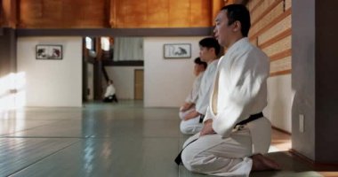 Asyalı adam, sınıf ve salon spor salonunda ustalaşmak için saygı, selam ya da onur için dojo 'da eğil. Karate grubunda erkek ya da grup görgü kuralları, tutum ya da dövüş sanatlarında birlikte hareket etmek için yerde eğiliyor..