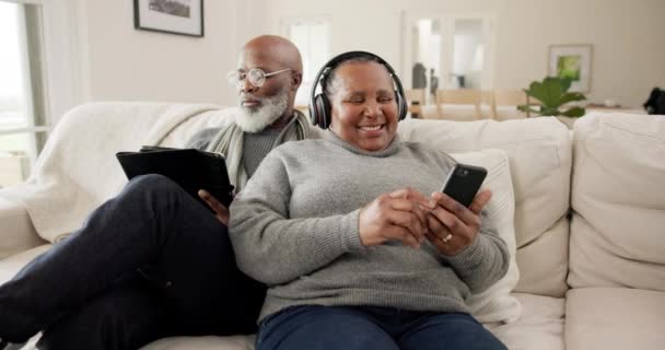 老夫妇 手机和笔记本电脑 沙发上的耳机 流媒体音乐和社交媒体为技术的快乐 老年男子和妇女播客放松 体育新闻和订阅 — 图库视频影像