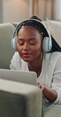 Müzik, kulaklık ve siyah kadın evdeki kanepede dizüstü bilgisayarda, rahatlamak için ses veya ses dinleyin. Gülücük, radyo ve Afrikalı insan bilgisayarda kanepede, şarkı çevrimiçi ya da internet teknolojisinde.