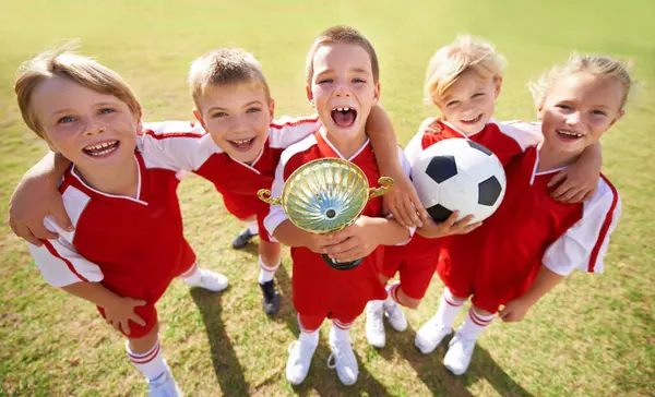 Kids, soccer team and portrait with cup, boys and girls with victory, support or solidarity. Achievement, sports and friendship, together and happy for win, ready for game or physical activity.