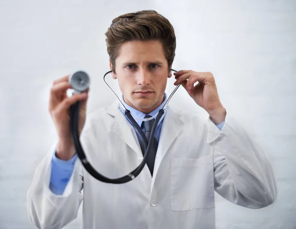 Serious, portrait and man doctor with stethoscope in his office for medical consultation at hospital. Listen, career and professional young male healthcare worker or intern at medicare clinic