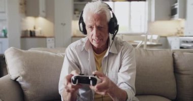 Oyun kumandası, kulaklık ve yaşlı adam video oyununda, fantezi roketatarında ya da dijital etkileşimli eğlencede kaybediyor. Oturma odası koltuğu, hayal kırıklığına uğramış ve olgun bir insan. Oyuncuların evdeki yenilgisine kızgın..