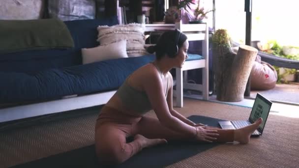 헤드폰과 노트북과 아시아 클래스 온라인 집에서 피트니스와 건강에 다리를 스트레칭 — 비디오