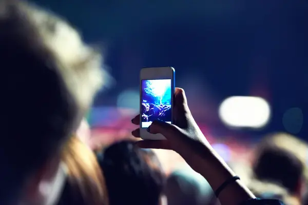 Woman, hand and smartphone for picture at concert with post, social media or recording of show. Closeup, female person and mobile app for sharing on internet for music, event or festival with crowd.