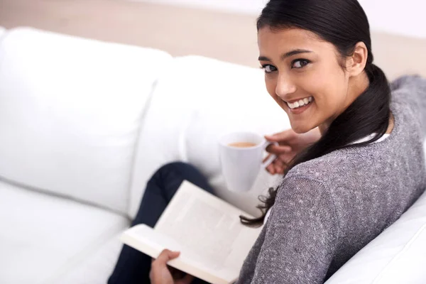 Woman, book and coffee on sofa for reading, learning and education in literature, language or knowledge. Portrait of Mexican student, relax with tea and living room with novel, fiction or happy story.