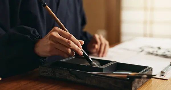 Hands, brush in ink for writing and Japanese calligraphy or ancient script for art and inkstone. Asian creativity, black paint and vintage tools, paintbrush and person with traditional stationery.