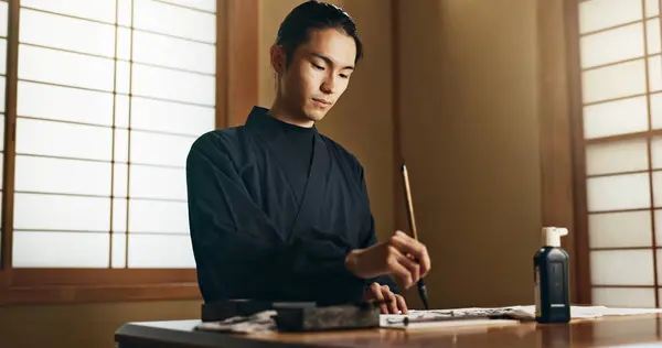 Calligraphy, ink and traditional Japanese man with paper for letters, notes and text for documents or script. Creative, writer and person with paintbrush, tools and desk for art, writing and culture.