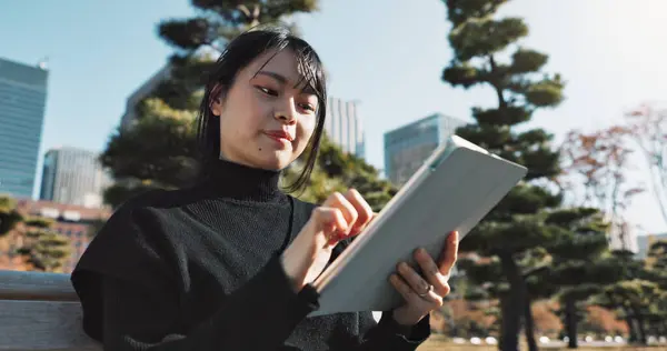 Happy asian woman, tablet and research at park in city for social media or outdoor networking. Female person smile with technology in relax for online search, reading or communication in nature.