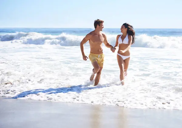 Holding hands, waves and happy couple running on beach for holiday adventure together on tropical island with care. Love, man and woman on ocean vacation with fun, romance and smile on travel in Bali.