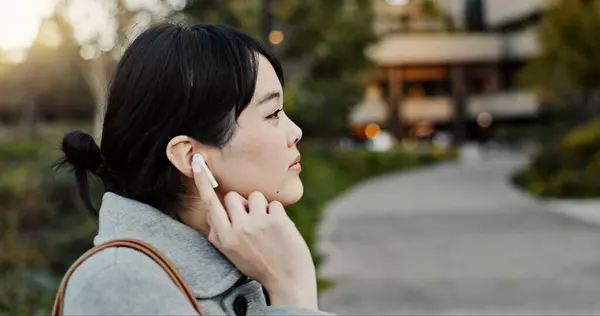 Japanese woman, earphones and walk in city with listening, music and streaming subscription on road. Girl, person and audio tech for podcast, radio and sound with travel on metro sidewalk in Tokyo.