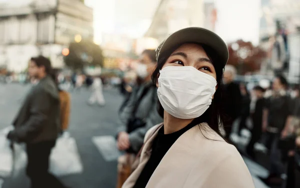 City, japan and woman in travel with face mask for health and walking in town. Covid compliance, safety for wellness and female person outdoors with facial protection for corona virus pandemic.