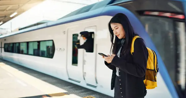 Asian woman, phone and train for travel, communication or social media at railway station. Female person smile with backpack or bag on mobile smartphone waiting for transportation, trip or traveling.