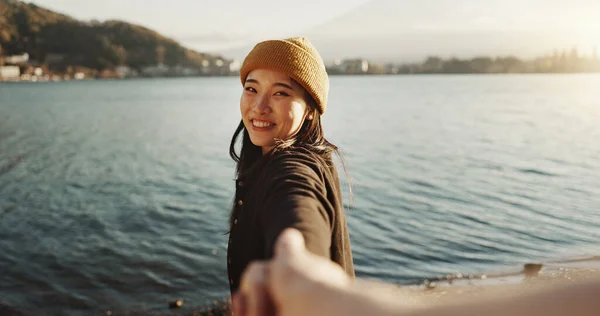 Happy, face and a couple holding hands at the beach for love, date or travel together for holiday. Nature, walking and portrait of a Japanese girl with a smile and leading a person to water or a lake.