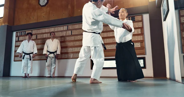 Aikido, sensei and Japanese students with discipline, fitness and action in class for defence or technique. Martial arts, people or fighting with training, uniform or confidence for culture and skill.
