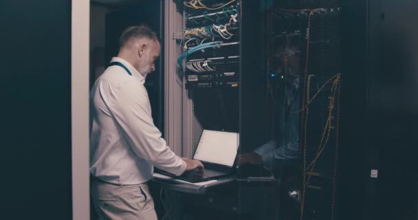ウェブアップデートのためのデジタルストレージのラップトップ ネットワークメンテナンスとエンジニアのためのソフトウェアを持つデータセンターの成熟した男 コンピュータが付いているサーバー部屋の技術的なスクリーン システム管理および技術者 — ストック動画