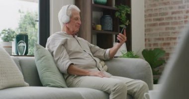 Kulaklıklar, ev ve yaşlı adam akıllı telefonlu, müzik yayınlayan ve oturma odasında radyo dinleyen. Bir dinlenme odasında emekli ve cep telefonu, kulaklığı ve uygulaması olan yaşlı bir adam..
