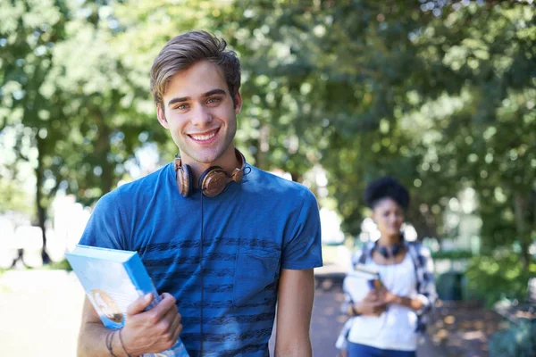 College, student and portrait of happy man on campus to study on scholarship for education. University, academy and person with book, headphones and walking with smile in park at school after class.