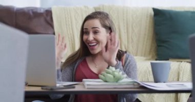 Happy, dizüstü bilgisayar ve kadın oturma odasında iletişimi selamlamak için el sallıyor. Gülümse, teknoloji ve Kanadalı genç bir kadın evdeki bilgisayarla sanal sohbet ediyor.