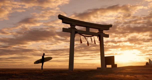 鳥居ゲート サンセット サーフボード オレンジ色の空と日本での旅の冒険 神道建築 アジア文化 落ち着いたビーチ — ストック動画