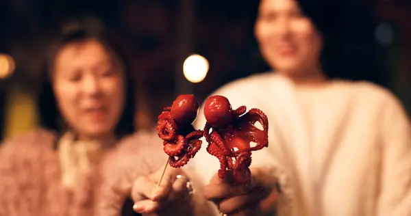 Women, Japan and travel street food at night for octopus delicacy, culture or traditional. Female people, snack and stick for tourism eating experience or cuisine in town for taste, dinner or holiday.