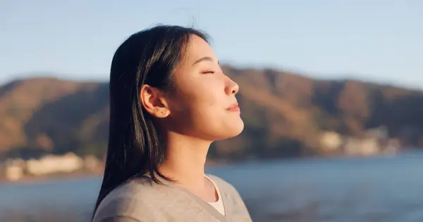 Japanese woman, breathing and peace outdoor, lake or ocean with travel, holiday and mindfulness in nature. Wellness, adventure and care free at beach in Japan, calm with freedom and positivity.