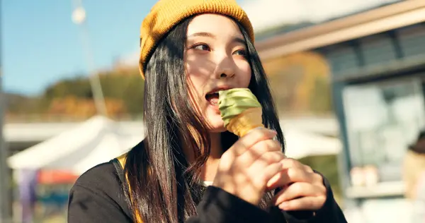 Japanese woman, ice cream and eating in city, summer and walk with thinking, memory or ideas on vacation. Girl, person and gelato for food, dessert and vision with taste, tourism and happy in Tokyo.