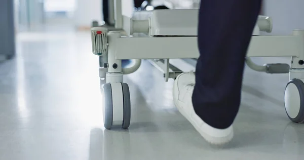 Healthcare, doctor and push bed in hospital for surgery, emergency or medical problem in corridor. Medicine, professional and nurse feet with stretcher for wellness, service and risk in clinic or job.