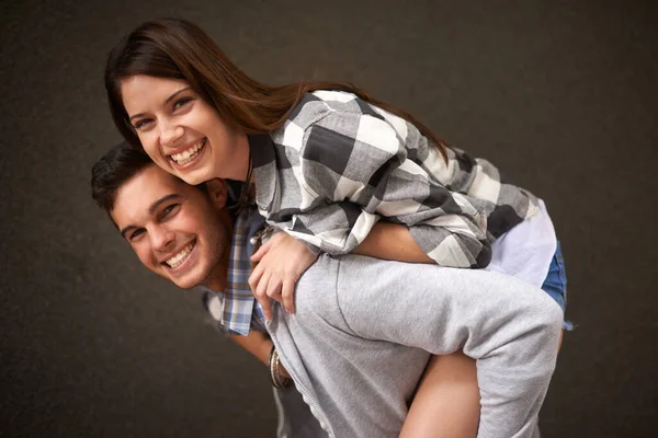 Smile, hug and portrait of couple piggyback ride, bond and having playful fun isolated on grey background. Support, embrace and young silly man, woman or people happy for funny game with partner.