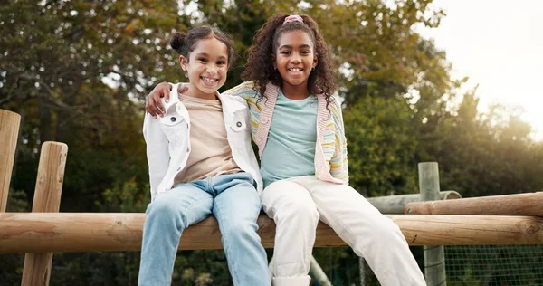 Friends, happy and children hug in park on jungle gym for bonding, childhood and having fun on playground. Friendship, outdoors and portrait of young girls embrace for playing, freedom and adventure.
