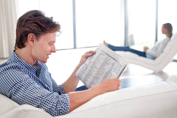 Man, newspaper and reading on sofa with relax for story, article or information with smile in living room. Person, news and morning routine on couch with print media or knowledge for break in lounge.