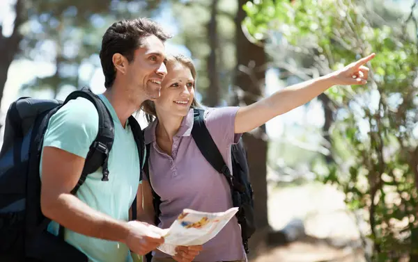 Couple, hiking in nature and map for direction, documents guide or location information of forest travel or journey. Man and woman trekking with infographics, search woods and pointing to destination.