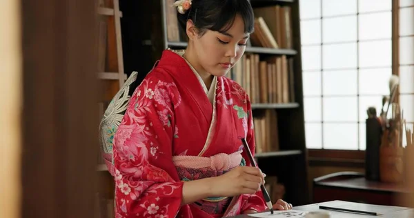 Calligraphy, writing and traditional Japanese woman in home for script, paper and documents. Creative, Asian culture and person with vintage paintbrush, ink and tools for art, font and text in house.