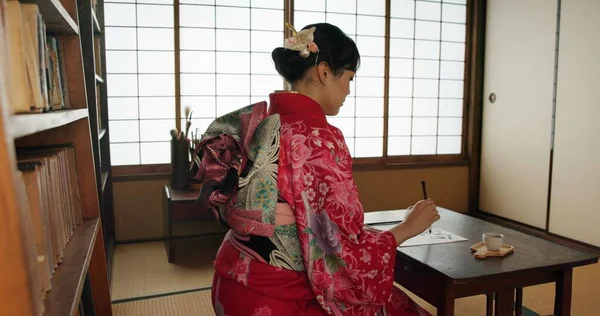 Traditional, writing and Japanese woman in home for script on paper, documents or page on desk. Creative, Asian culture and person with vintage paintbrush, ink and tools for calligraphy, font or text.
