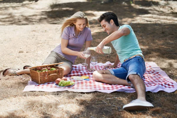 Couple, picnic and champagne outdoor in nature or park for celebration of love, summer date and valentines day. Young people with food, fruits and drink bottle or wine glasses in woods on anniversary.