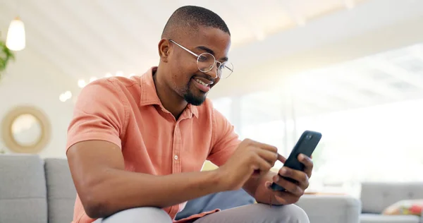Happy, typing and a black man with a phone on the sofa for social media, connection or communication. Smile, relax and an African person with a mobile for an app, email or notification in a house.