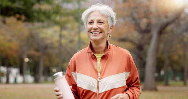 Fitness, senior woman and walking at park for healthy body, wellness or exercise with bottle. Smile, workout and elderly athlete outdoor, nature or garden for cardio, sport and travel for retirement.