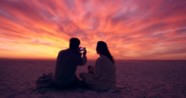 Gün batımı, gökyüzü ve sahilde fotoğraf, manzara ve aşk ve evlilik için tatile çıkan insanlar için akıllı telefonlu bir çift. Hayat arkadaşı, fotoğraf çekiyor ve hafızasına güveniyor ve tarihle bağlılık gösteriyor..